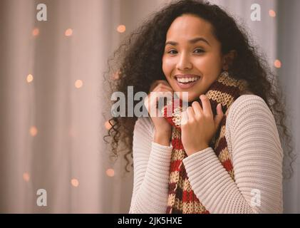 Kalte Nächte, warme Herzen. Porträt einer jungen Frau, die zu Weihnachten zu Hause einen Schal trägt. Stockfoto