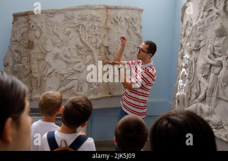 Bukarest, Rumänien. 30.. Juli 2022. Ein Mann erklärt den Kindern die Bedeutung eines nachgebildeten Fragments der Traian-Säule aus Rom während einer Tour durch das Nationale Geschichtsmuseum in Bukarest, Rumänien, am 30. Juli 2022. Quelle: Cristian Cristel/Xinhua/Alamy Live News Stockfoto