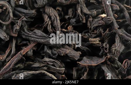 Hochwertiger schwarzer Tee mit losen Blättern als Hintergrund. Textur von trockenen schwarzen Teeblättern. Extrem-Makromodus Stockfoto