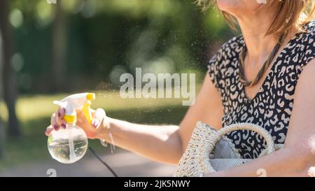 Frau kühlt sich in einem öffentlichen Park wegen der hohen Sommertemperaturen mit einem Wasserstrahl ab. Stockfoto