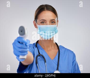 Eine junge Krankenschwester hält ein digitales Thermometer vor einem Studioraum. Stockfoto