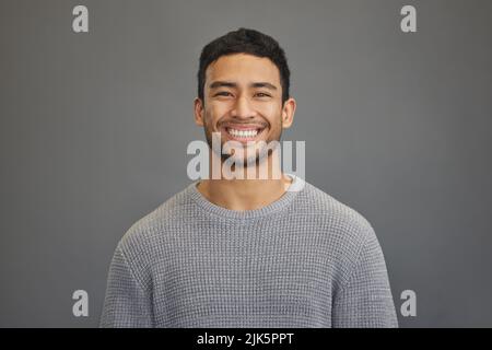 Ein Lächeln ist das beste Geschenk, das Sie jemandem schenken können. Ein hübscher junger Mann, der vor einem grauen Hintergrund steht. Stockfoto