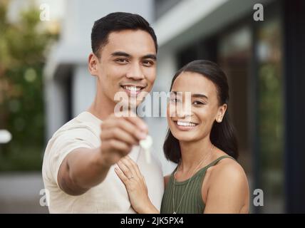 Werfen wir einen Blick ins Innere. Ein junges Paar, das den Schlüssel zu ihrem neuen Zuhause hält. Stockfoto