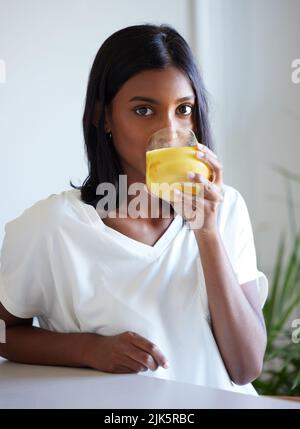 Es wird ein fruchtbarer Tag. Eine schöne junge Frau, die zu Hause ein Glas Orangensaft trinkt. Stockfoto