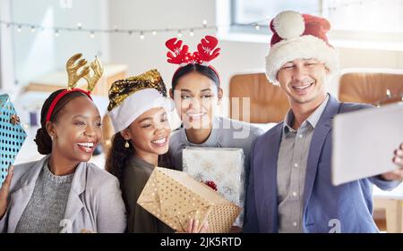 Die Weihnachtsstimmung im Büro. Eine Gruppe von Kollegen, die ein Selfie machen, während sie Weihnachten bei der Arbeit feiern. Stockfoto