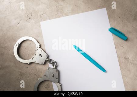 Handschellen, ein leeres Blatt Papier und ein Stift auf dem Tisch Stockfoto