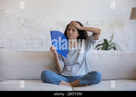 Müde Lateinerin schwenkt Handventilator aus Papier, um die Luft zu kühlen Stockfoto