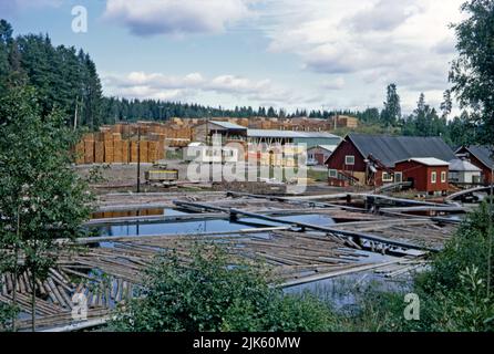 Die Holzindustrie in Norwegen im Jahr 1970. Die abgeschnittenen Holzstämme schweben in der Holzmühle zur Verarbeitung bereit. Das fertige, abgeschnittene Holz wird auf der Rückseite zum Versand gestapelt. Dieses Bild stammt von einer Amateur-35mm-Farbtransparenz – einem Vintage-1970s-Foto. Stockfoto