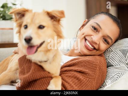 Er hält mich IMMER für schön. Porträt einer schönen jungen Frau, die sich mit ihrem Hund zu Hause auf der Couch entspannt. Stockfoto