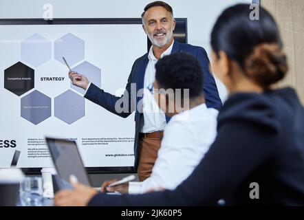 Erklärung der wichtigsten Strategien für sein Team. Ein reifer Geschäftsmann, der seinen Kollegen in einem Büro eine Präsentation gibt. Stockfoto