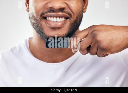 Bärte sind sehr trendig. Studioaufnahme eines jungen Mannes, der seine Gesichtsbehaarung vor weißem Hintergrund putzt. Stockfoto