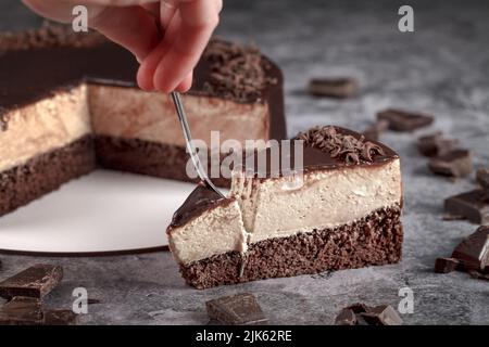 Ein Stück Cappuccino-Mousse mit einer Gabel auf grauem Hintergrund, verziert mit schwarzer geriebener Schokolade. Foto für Menü oder für Werbung confec Stockfoto