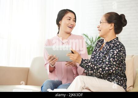 Eine ältere asiatische Frau und ihre Erwachsene Tochter mit einem digitalen Tablet diskutieren über Neuigkeiten Stockfoto