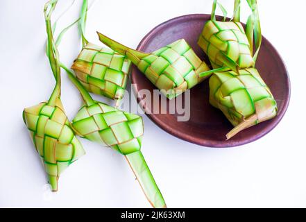 Ketupat in Steingutplatte isoliert auf weißem Hintergrund. Ketupat (Reisknödel) ist ein Essen, das serviert wird, wenn idhul fitri (eid mubarak) in Indonesien, Fr. Stockfoto