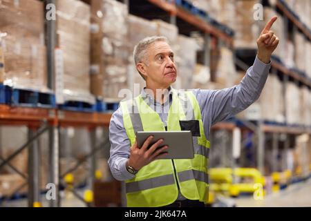 Sammeln von Daten über alle aktuellen Lager und Waren. Ein reifer Mann mit einem digitalen Tablet während der Arbeit in einem Lager. Stockfoto