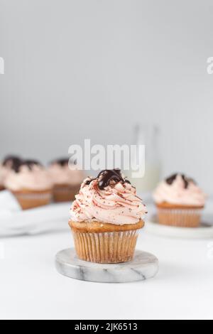 Vanillekuchen mit einem hohen Strudel rosa Zuckerguss, Schokoladenglasur und einem Keks, einfarbiger Cupcake mit pastellrosa Buttercreme mit Schokolade und Stockfoto