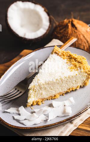 Stück Kokosnuss-Käsekuchen auf einem Teller mit frischer Kokosnuss. Stockfoto