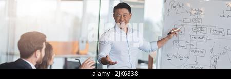 Ein reifer asiatischer Trainer oder Redner präsentiert bei einem Meeting verschiedene Geschäftsleute auf einem Flipchart Stockfoto