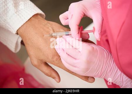 Frau Hände machen eine Beauty-Injektion zu einem Mann Arm Stockfoto