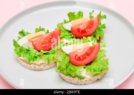 Reiskuchen-Sandwiches mit Tomaten, Salat und Ei auf weißem Teller. Einfaches Frühstück. Diät-Essen. Schnelle und gesunde Sandwiches. Knäckebrot mit leckerer Füllung. Gesunder Ernährungs-Snack Stockfoto