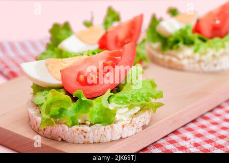 Reiskuchen-Sandwiches mit Tomaten, Salat und Ei auf Holzbrett. Einfaches Frühstück. Diät-Essen. Schnelle und gesunde Sandwiches. Knäckebrot mit leckerer Füllung. Gesunder Ernährungs-Snack Stockfoto