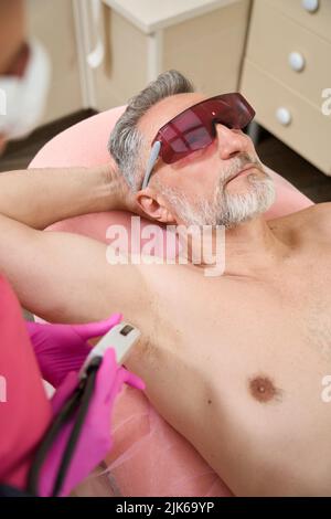 Weibliche Hände des Arztes führen Laser-Haarentfernung in Achselhöhlen Stockfoto