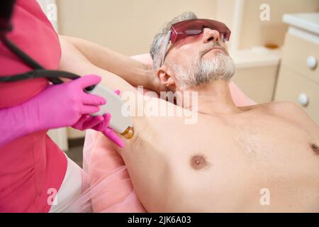 Weibliche Hände des Dermatologen führen Laser-Haarentfernung in den Achselhöhlen Stockfoto
