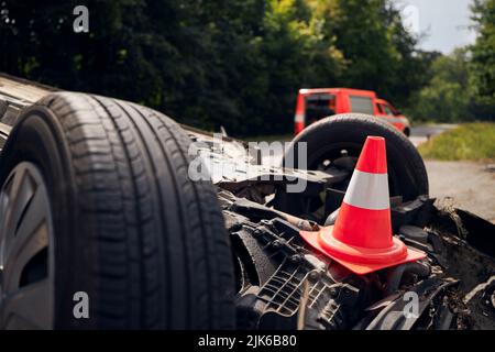 Beschädigtes Fahrzeug auf dem Dach nach einem Unfall mit einem Feuerwehrfahrzeug. Selektiver Fokus auf den Verkehrskegel. Stockfoto
