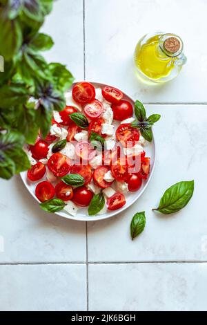 Caprese-Salade auf einem Teller unter einer Basilikumpflanze serviert Stockfoto