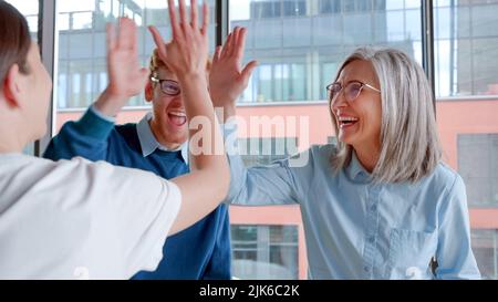 Fröhliche und begeisterte kreative Gruppe von Menschen, die ihre Hände hochheben und hohe fünf geben. Stockfoto