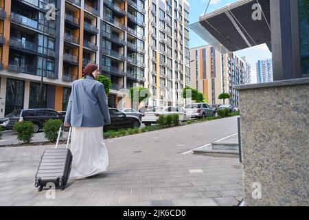 Eine Frau, die die Straße entlang läuft und einen Koffer auf Rädern hält Stockfoto