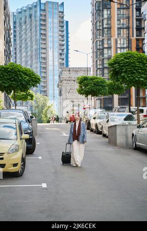 Eine arabische Frau geht mit einem Koffer auf Rädern durch den Parkplatz Stockfoto