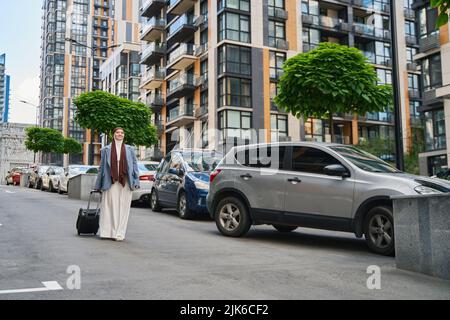 Die Frau in einem Hijab trägt einen Koffer auf Rädern Stockfoto