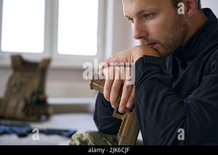 Ernsthafter Armeemann mit Waffe, der zu Hause sitzt Stockfoto