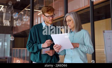 Reife Geschäftsfrau Lehre auf Dokumenten junge männliche Praktikantin im Büro Stockfoto