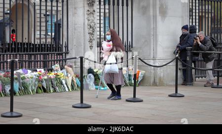 London, Großbritannien - 10. April 2021: Ältere Frau legt Blumen für den Tod von Prinz Philip, dem Herzog von Edinburgh, im Buckingham Palace in London