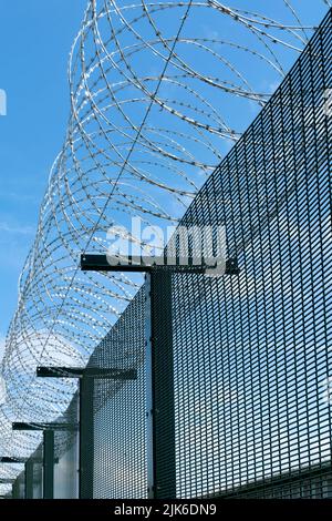 Das Bild zeigt ein Stachelband mit Stacheldraht, das sich an der Spitze eines Metallzauns aufwickelt. Der Draht ist eine sichere Abschreckung und bietet Sicherheit für das Gelände Stockfoto