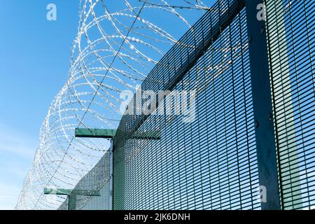 Das Bild zeigt ein Stachelband mit Stacheldraht, das sich an der Spitze eines Metallzauns aufwickelt. Der Draht ist eine sichere Abschreckung und bietet Sicherheit für das Gelände Stockfoto