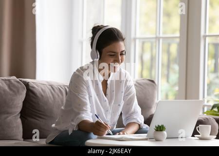 Glückliche junge indische Studentin im schnurlosen Headset beim Webinar Stockfoto