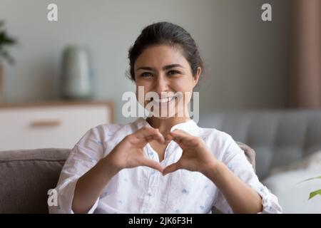 Glückliche hübsche junge indische Frau, die an der Brust verbundene Hände zeigt Stockfoto