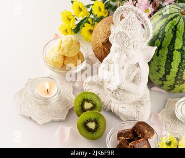 Urlaub in Ganesh Chaturth. Skulptur von ganesha mit Opfergaben, Früchten, Süßigkeiten, Blumen und Kerzen auf weißem Hintergrund. Lord Ganesha, Ganesh fest Stockfoto