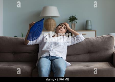 Erschöpftes junges indisches Mädchen, das sich heiß fühlt und sich auf der Couch ausruht Stockfoto