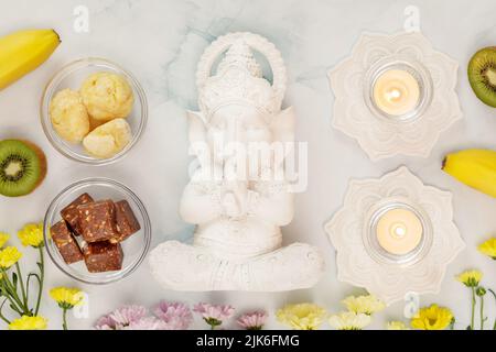 Ganesh Chaturth Urlaub. Skulptur von Ganesha mit Opfergaben, Früchten, Süßigkeiten, Blumen und Kerzen auf blauem Hintergrund. Lord Ganesha, Ganesh-Fest Stockfoto