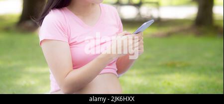 Glück junge asiatische Frau schwanger sitzen Videoanruf mit der Familie auf dem Smartphone im Park, Frau und positiv der Gesundheit Fruchtbarkeit, Mama mit smart Stockfoto