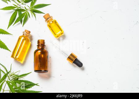 Cannabisöl in Glasflaschen und Cannabisblätter am weißen Tisch. Stockfoto