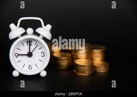 Weißer Wecker mit isolierten Goldmünzen auf dunklem Hintergrund. Platz und Geschäftskonzept kopieren. Stockfoto