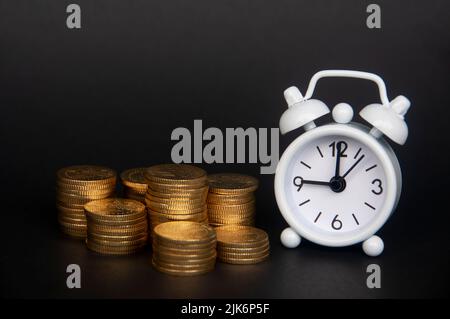 Weißer Wecker mit isolierten Goldmünzen auf dunklem Hintergrund. Platz und Geschäftskonzept kopieren. Stockfoto