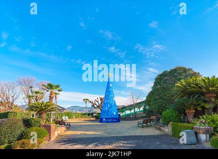 nagasaki, kyushu - 13 2021. dezember: Blauer weihnachtsbaum mit einem goldenen Stern unter dem blauen Himmel von Nagasaki, umgeben von den Palmen der Stockfoto