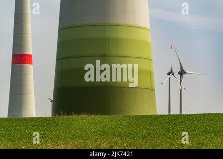 Nahaufnahme des mächtigen Turmsockels einer Windkraftanlage auf einem grünen Feld, mit mehreren anderen Windkraftanlagen im Hintergrund Stockfoto