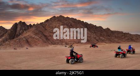 Ein nicht erkennbarer Mann auf einem roten Quad in der ägyptischen Wüste von Sharm el-Sheikh bei Sonnenuntergang Stockfoto